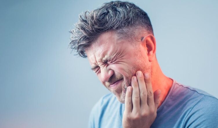 Vyras laiko skausmingą dantį, rodo, kad jis patiria stiprų dantų skausmą ir ieško būdų, kaip palengvinti skausmą.